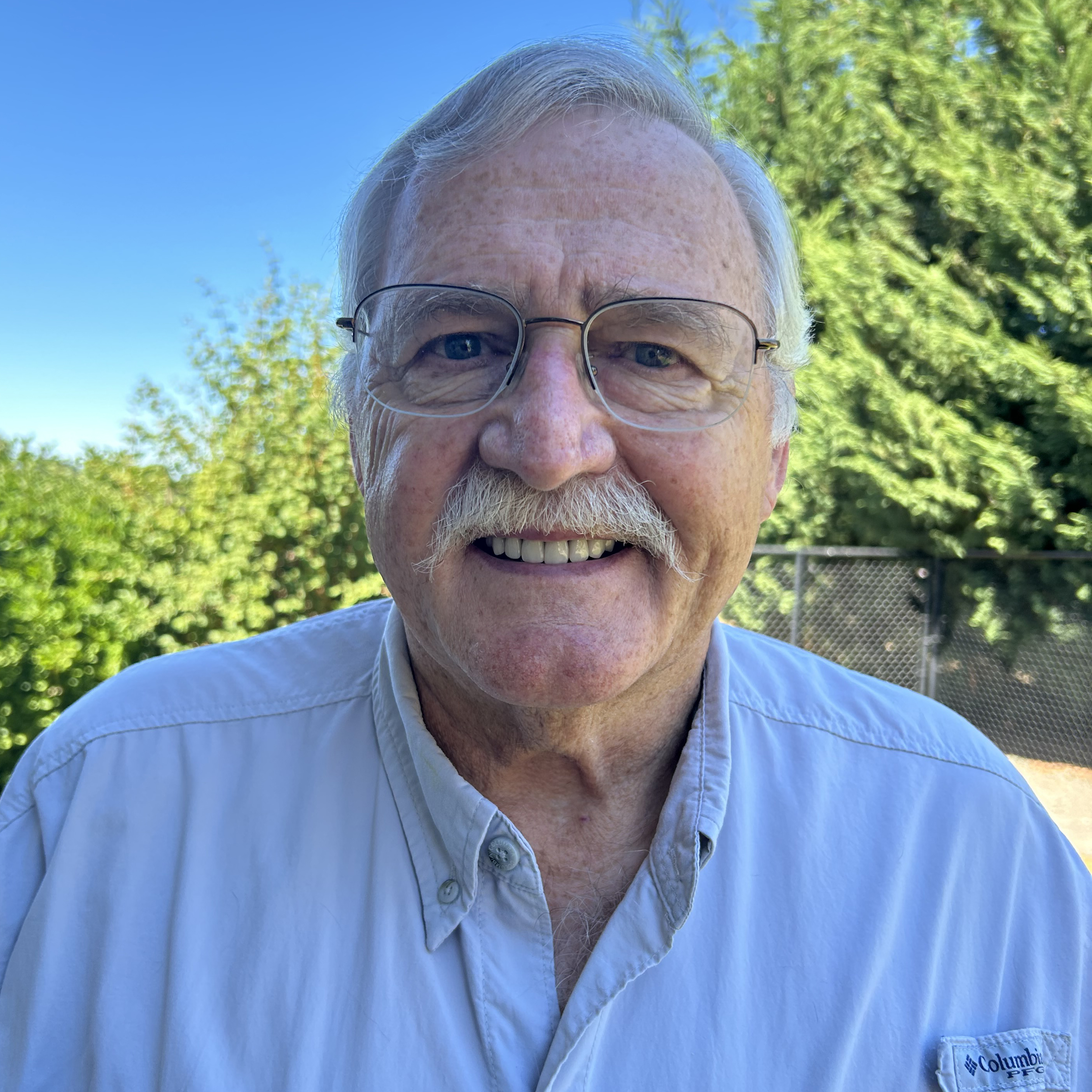 A man wearing a button-up shirt outdoors during summer.