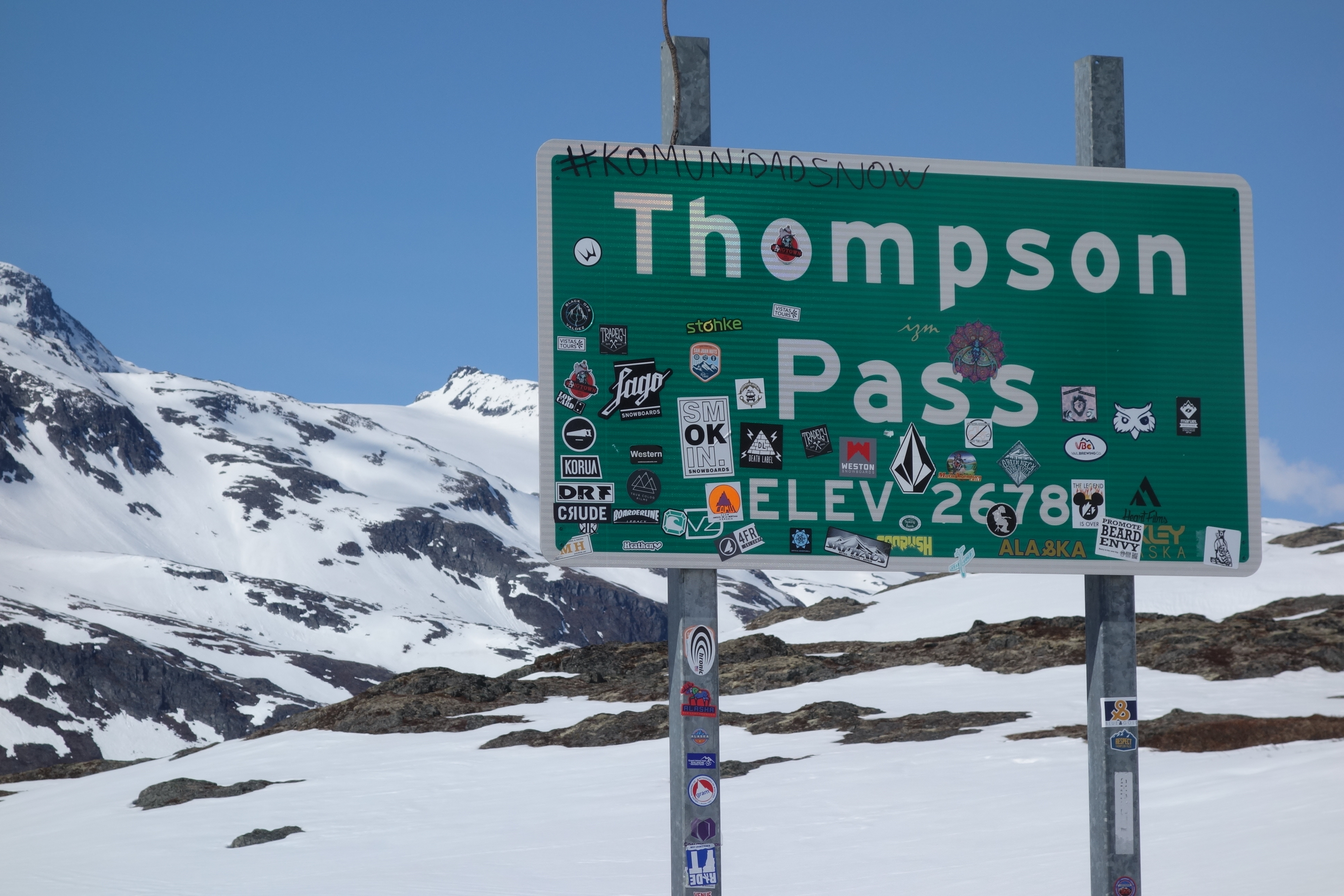 a road sign for Thompson Pass covered with grafitti and stickers, shown in a snowy landscape