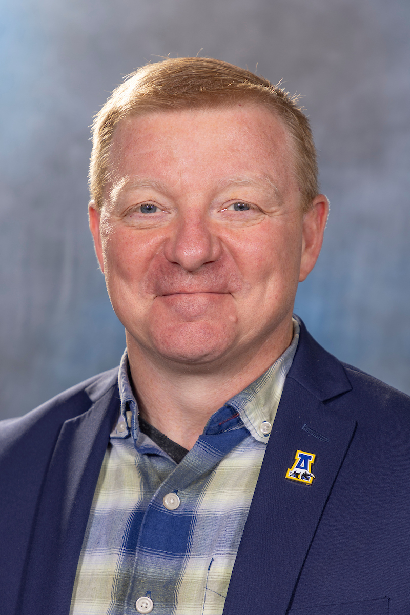 A man wearing a blue and yellow plaid shirt with a dark blue business jacket.