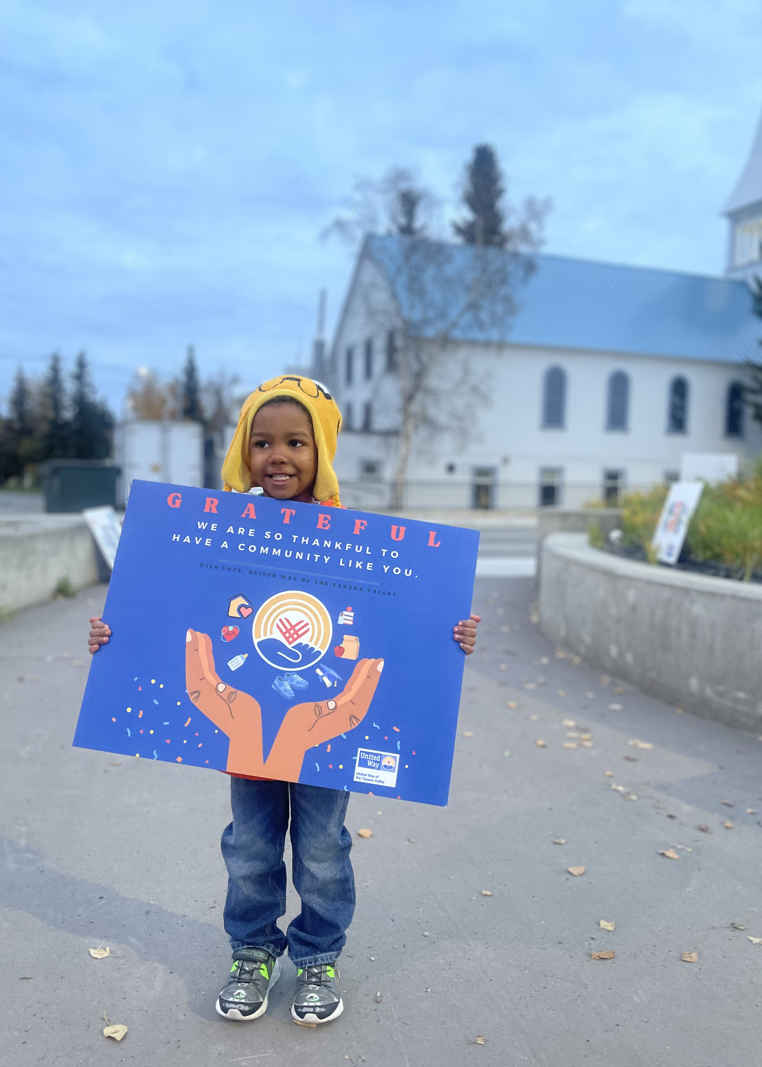 A child holding a poster that reads, Grateful: we are so thankful to have a community like you.