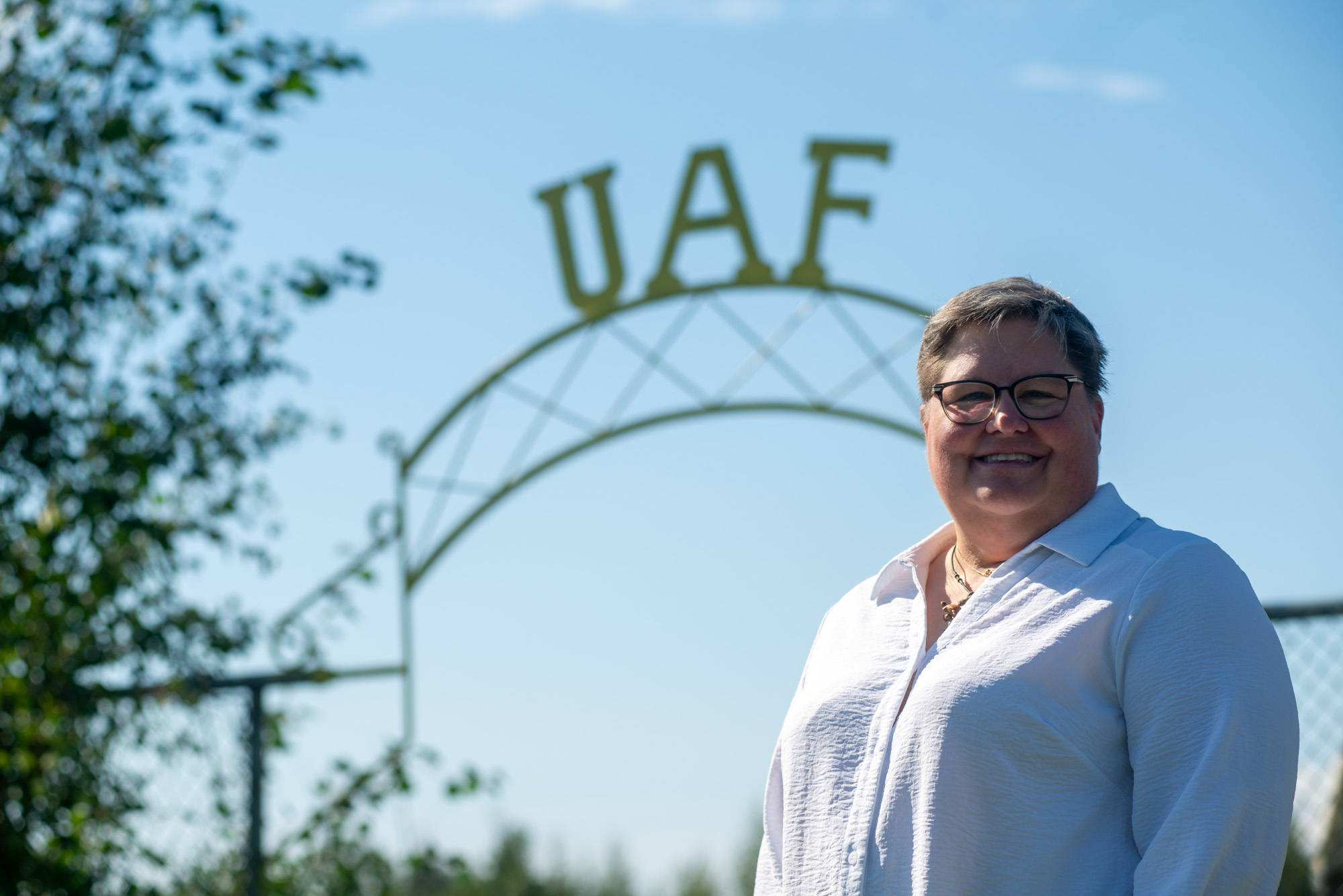 A smiling woman, Jodie Anderson, stands in front of an arch with the letters UAF on top