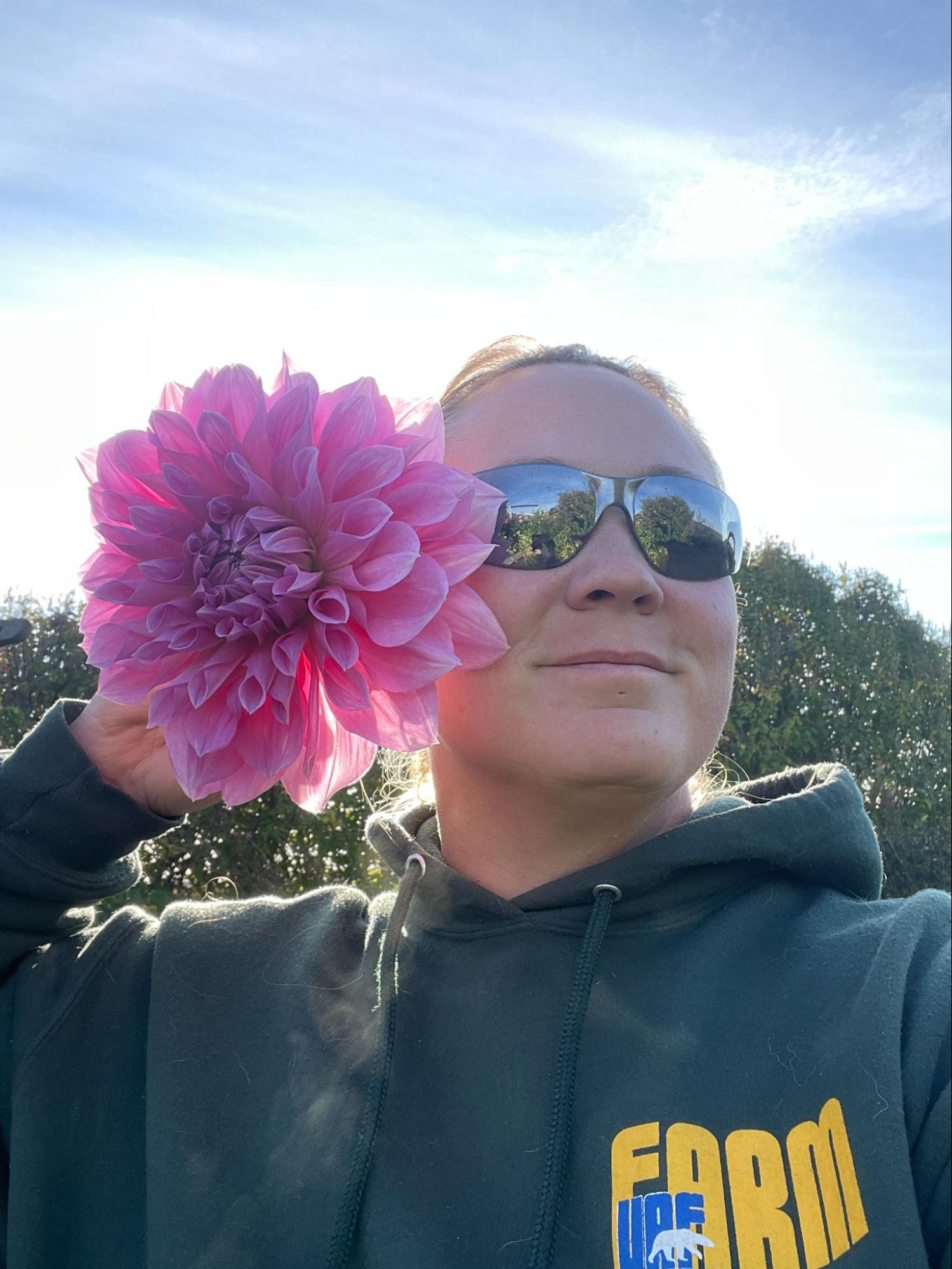 A woman holds a large pink peony up to her face with the sun shining from behind