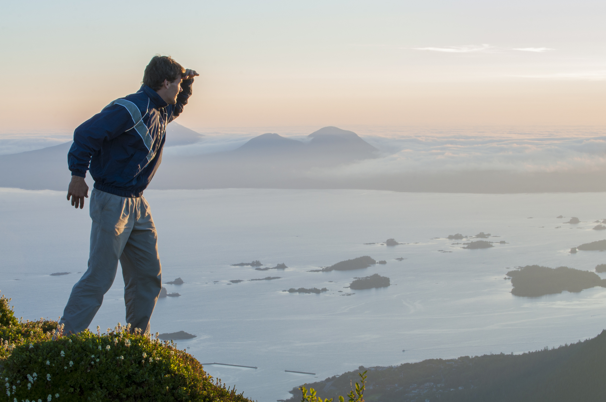 A youth stands on a mountain as the sun sets over an ocean inlet