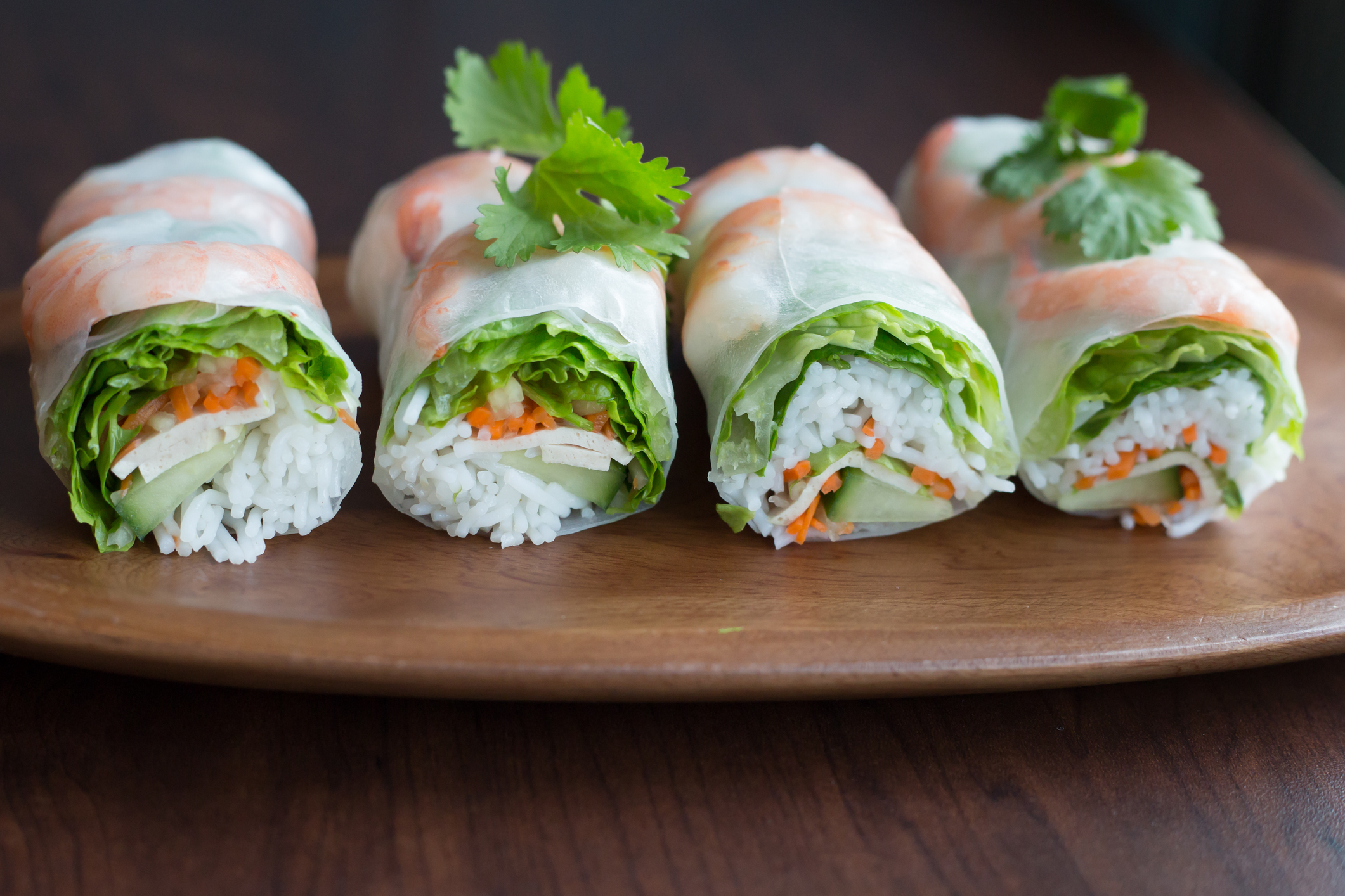Four fresh spring rolls filled with fresh vegetables laid out on a plate