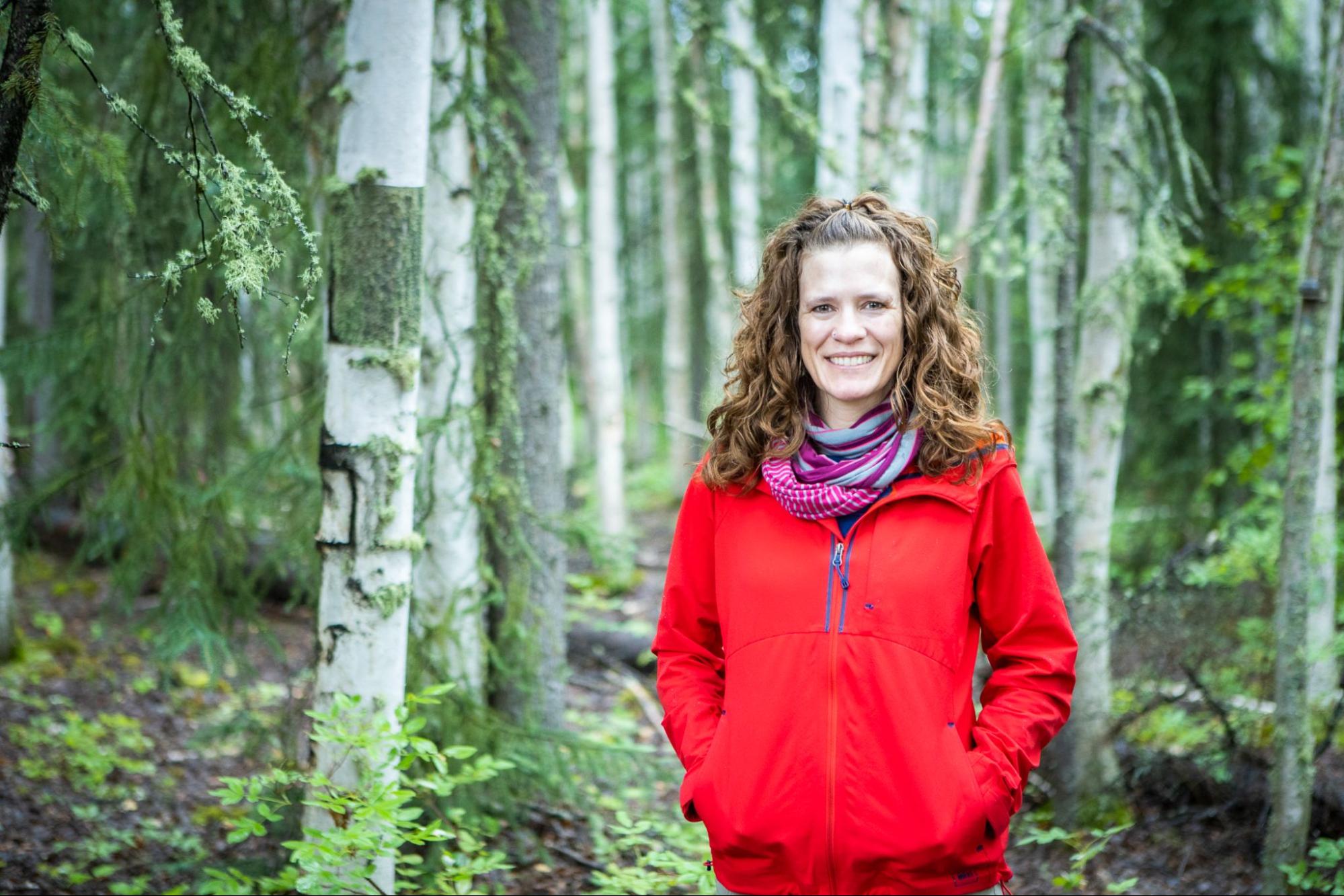 A woman in a red sweater, Jessie Young-Robertson, stands in a birch forest