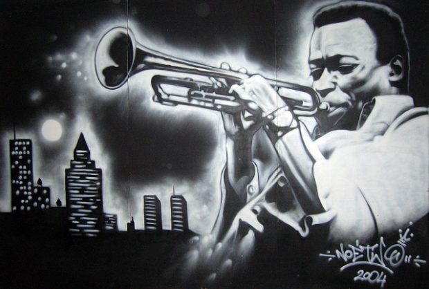 Black and white artistis rendering of Miles Davis playing his trumpet in front of the city skyline