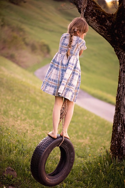 Young girl in a dress standing on a tire swing