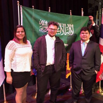 Students pose in front of the flag of Saudi Arabia at a Model UN conference