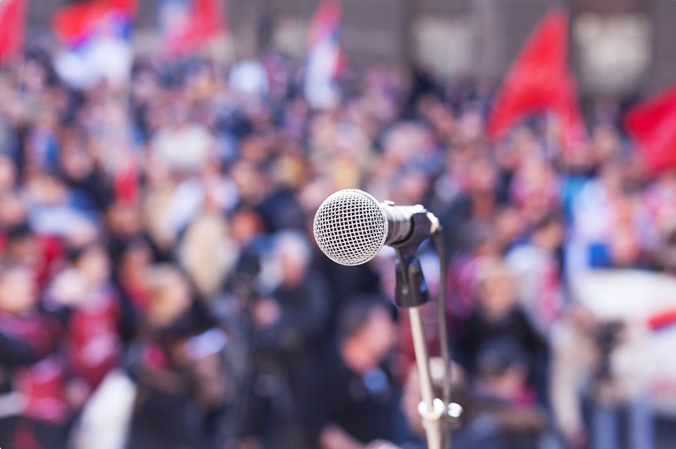 A microphone in front of a large crowd of people from the point of view of the speaker on stage | Stock image from Canva