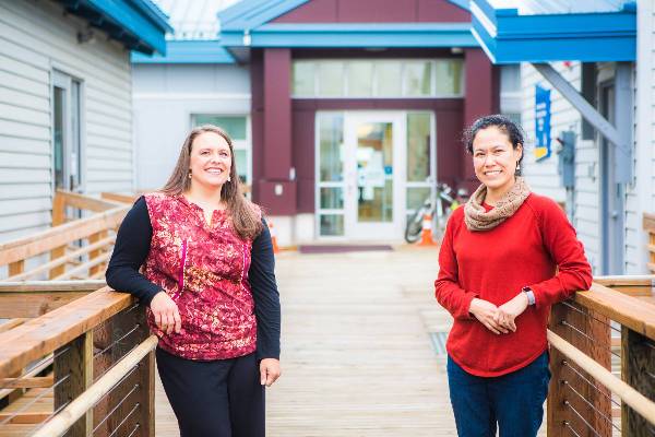 Two smiling women stand outside the Northwest Campus