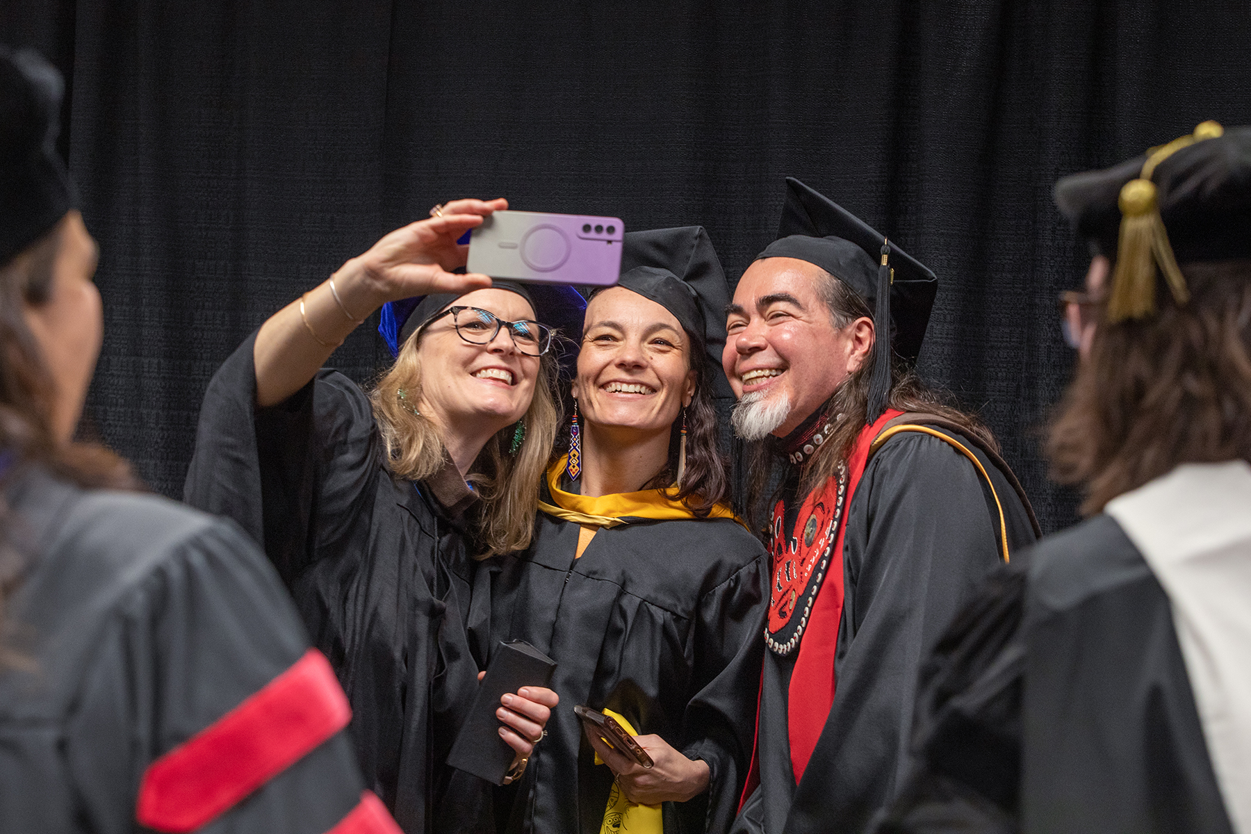 (from left) Carrie Baker, Professor and Associate Dean, College of Liberal Arts, Dept. of Theatre and Film, Maya Salganek, Director of FRAME and Associate Professor, Film/Video Arts, and Da-ka-xeen Mehner, Professor of Native Art and Department Chair, take a photo before the faculty processional during the University of Alaska Fairbanks 2023 Commencement Ceremony at the Carlson Center Saturday, May 6, 2023. | UAF Photo by Eric Engman