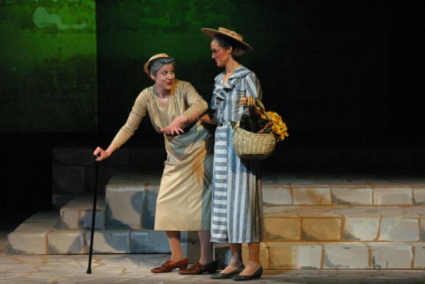 An elderly woman using a cane being assisted by another woman carrying a basket of flowers.