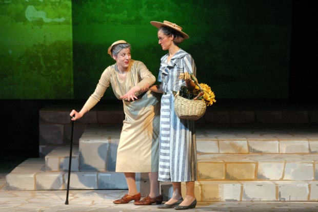 n elderly woman using a cane being assisted by another woman carrying a basket of flowers.
