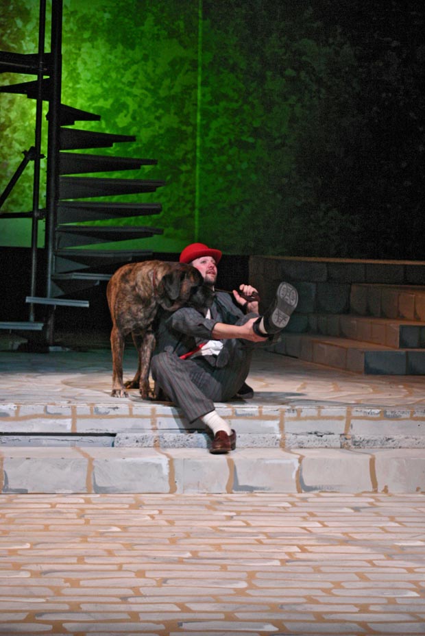 An unexpected moment of companionship captured on stage: a man adjusts his shoe as his loyal dog rests its head on his chest