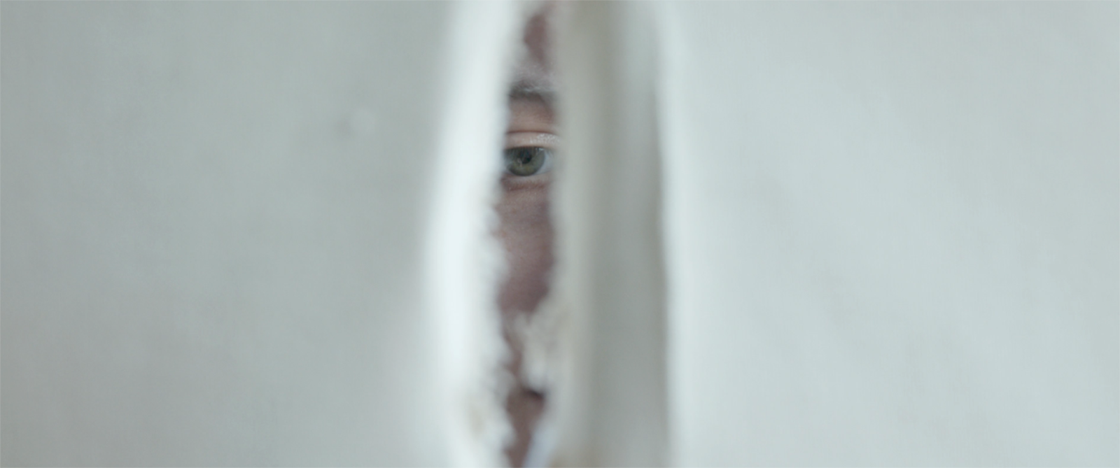 A downcast eye peers through a hole. Production still from 'Mend' a short film by JB Brown
