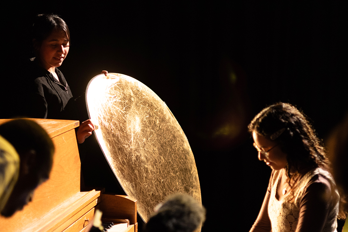 TAOS, Day 1, image 198 A crew member holds a reflecting dish towards Julieth Harvey (seated at the piano). Photo credit: Eric Marshall