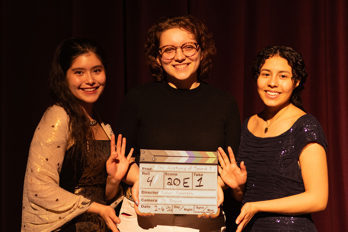 TAOS, Day 1, image 285 Taylor Kamrath, flanked by Na’ni’eezh Peter (left) and Julieth Harvey (right), holds a clapperboard from filming. Photo credit: Eric Marshall