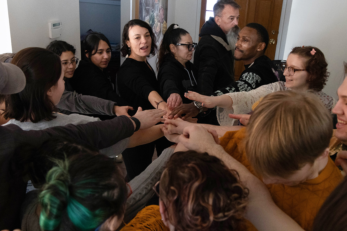 TAOS, Day 3, image 3 Cast and crew stand in a circle with hands together in the middle, ready to start the third day of filming. Photo credit: Eric Marshall