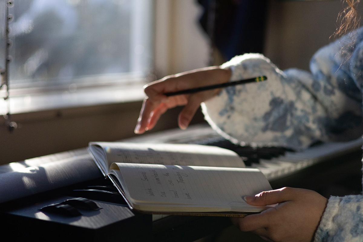TAOS, Day 4, image 34 Julieth Harvey's hand paused hovering over an open notebook. Photo credit: Eric Marshall