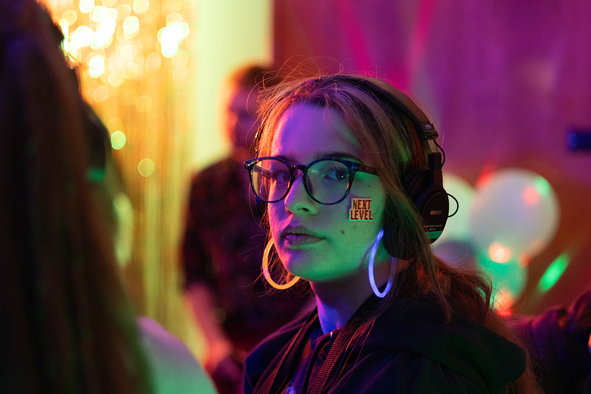 TAOS, Day 6, image 101 Madison Grapengeter in headphones with a "Level Up" sticker on their cheek on the set of The Anatomy of Sound. Photo credit: Eric Marshall