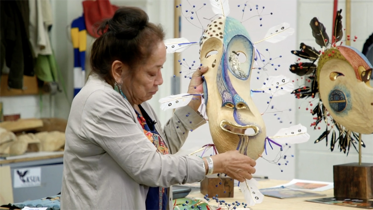 To Continue or Be Remembered Artist Kathleen Carlo displays a handcarved mask. Still from To Continue or Be Remembered