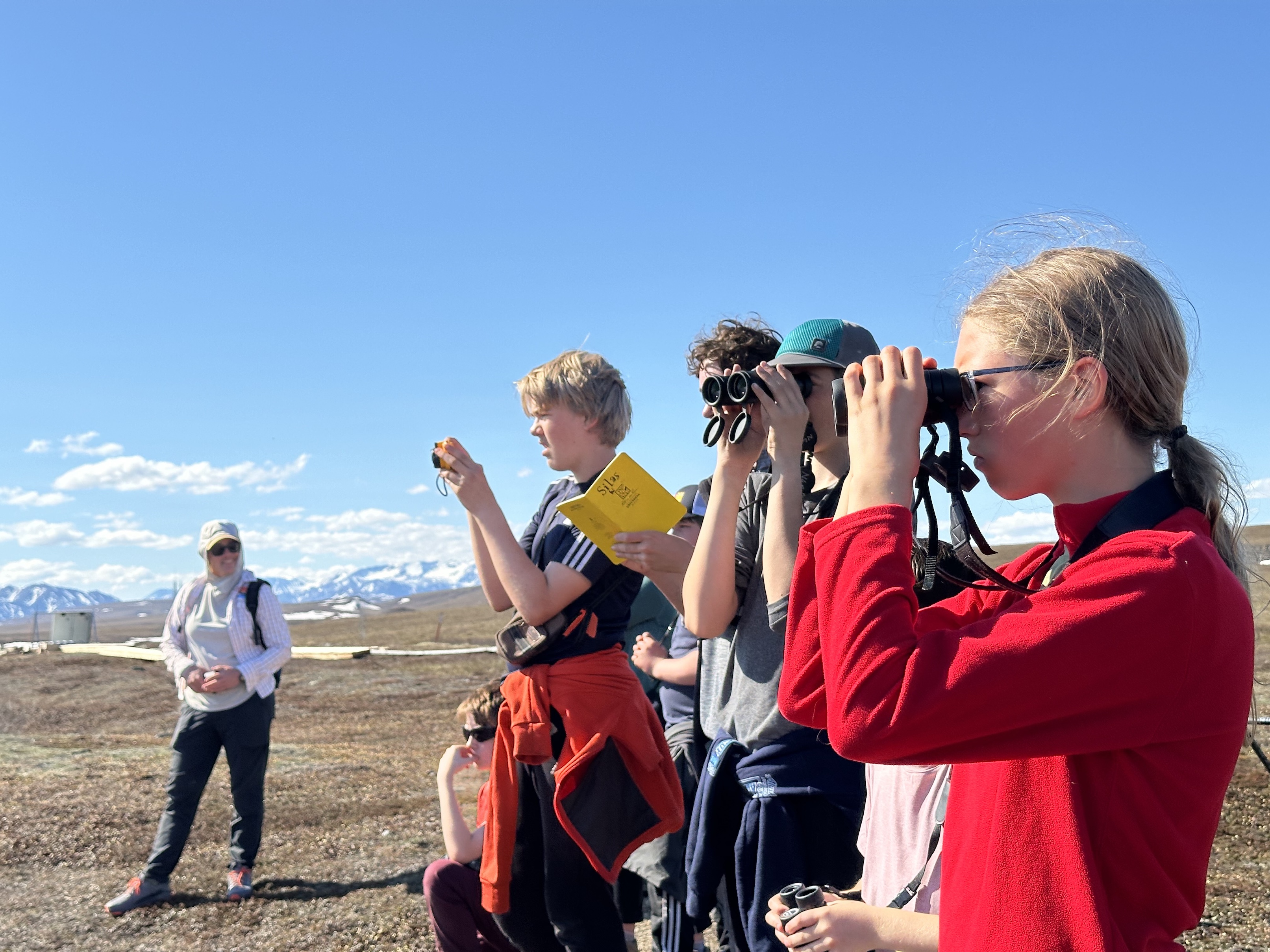 Middle school students scan the tundra for birds with binoculars
