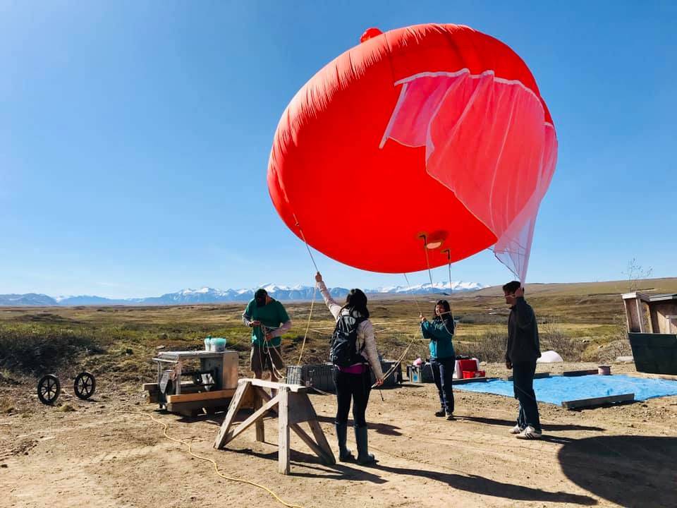 Four people launching a weather balloon with tundra and mountains in the background