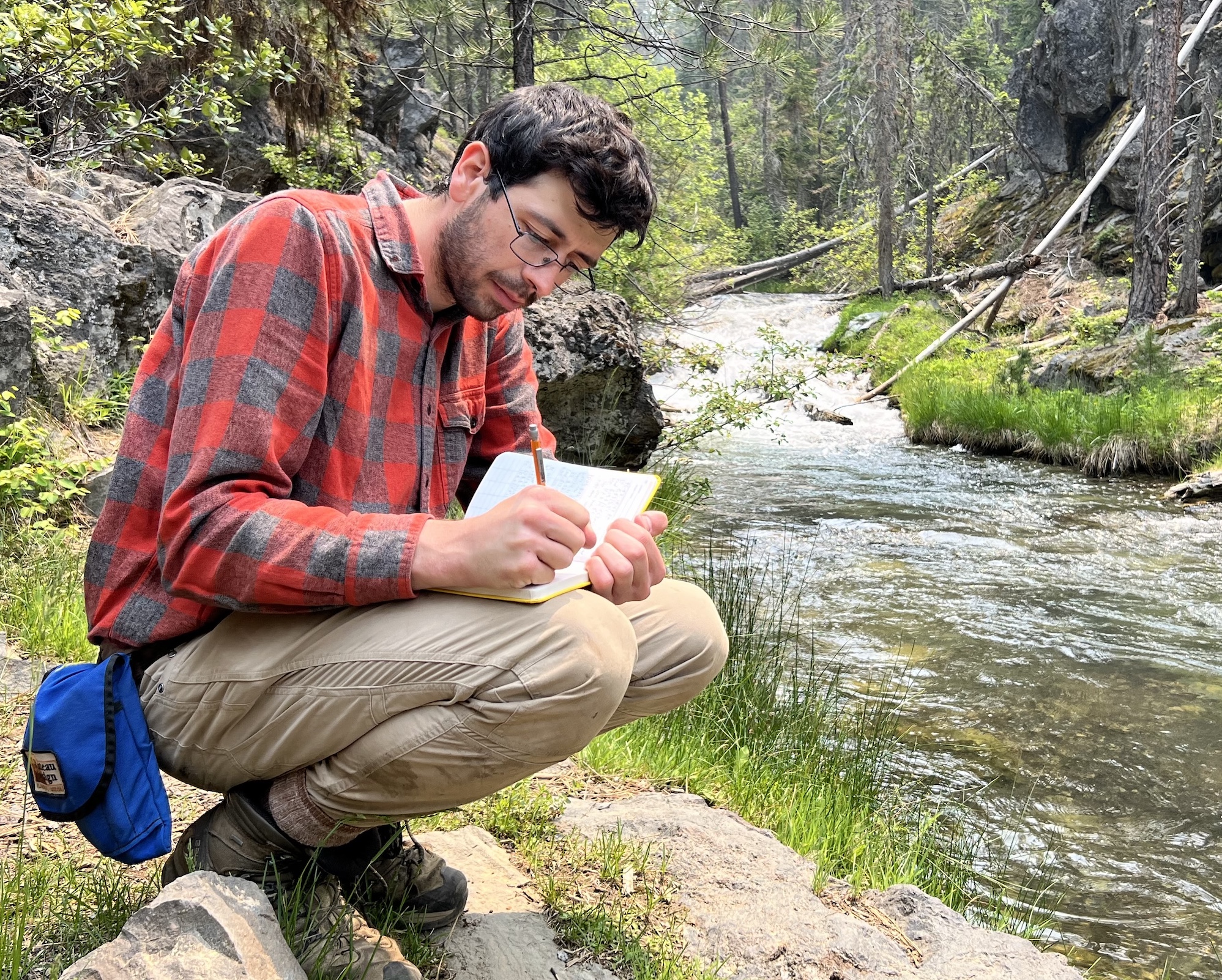 Preston Kemeny taking notes by a forest stream