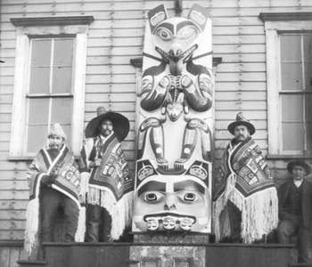 Four Chiefs of the Kogwanton clan in ceremonial regalia, posing next to Panting Wolf carving, during 1904 potlatch in Sitka