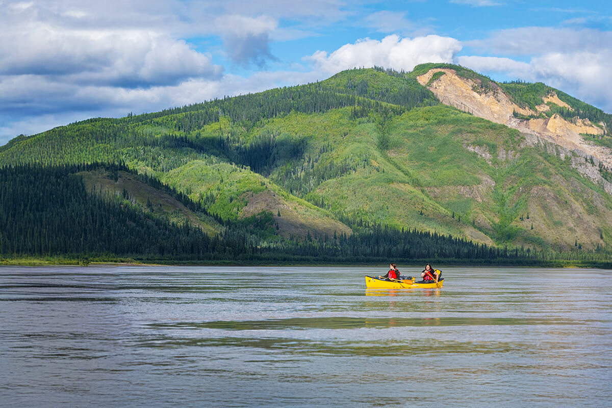 Students paddling a canoe on a river with a mountain rising the background