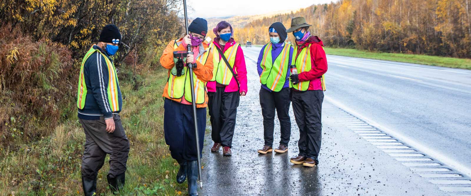 Students in masks and high-visibility safety vests conduct field work at a small landslide on the Steese Highway.
