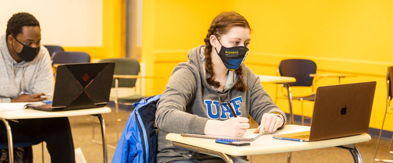 Students wearing masks and physically distance seated in a classroom at laptops