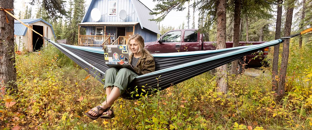 A student with a laptop studies while seated in a hammock outside their cabin in Fairbanks.