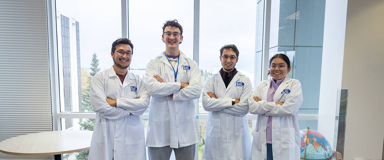A group of UAF Biomedical Learning and Student Training students pose in white lab coats.
