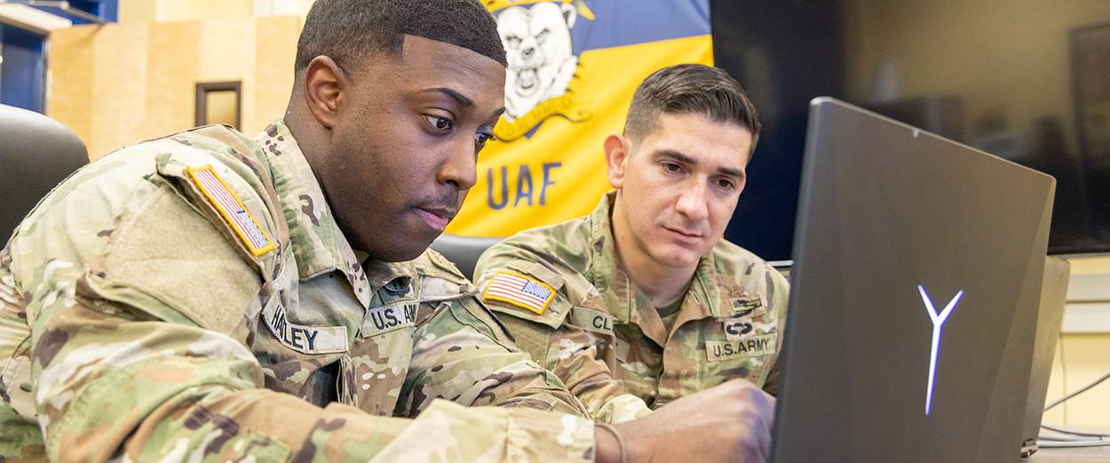 Two UAF ROTC students in uniform looking at a laptop screen