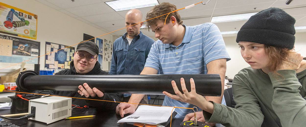 Students in a physics lab measuring sound frequencies with a speaker and a pipe
