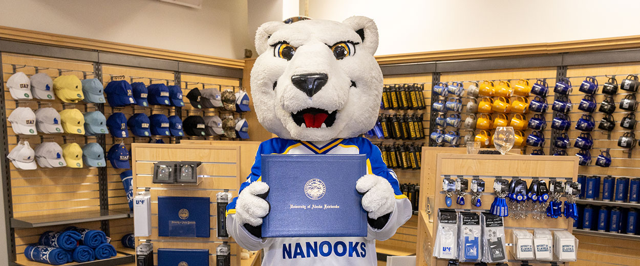 The Nook mascot poses with a diploma cover at the UAF Bookstore