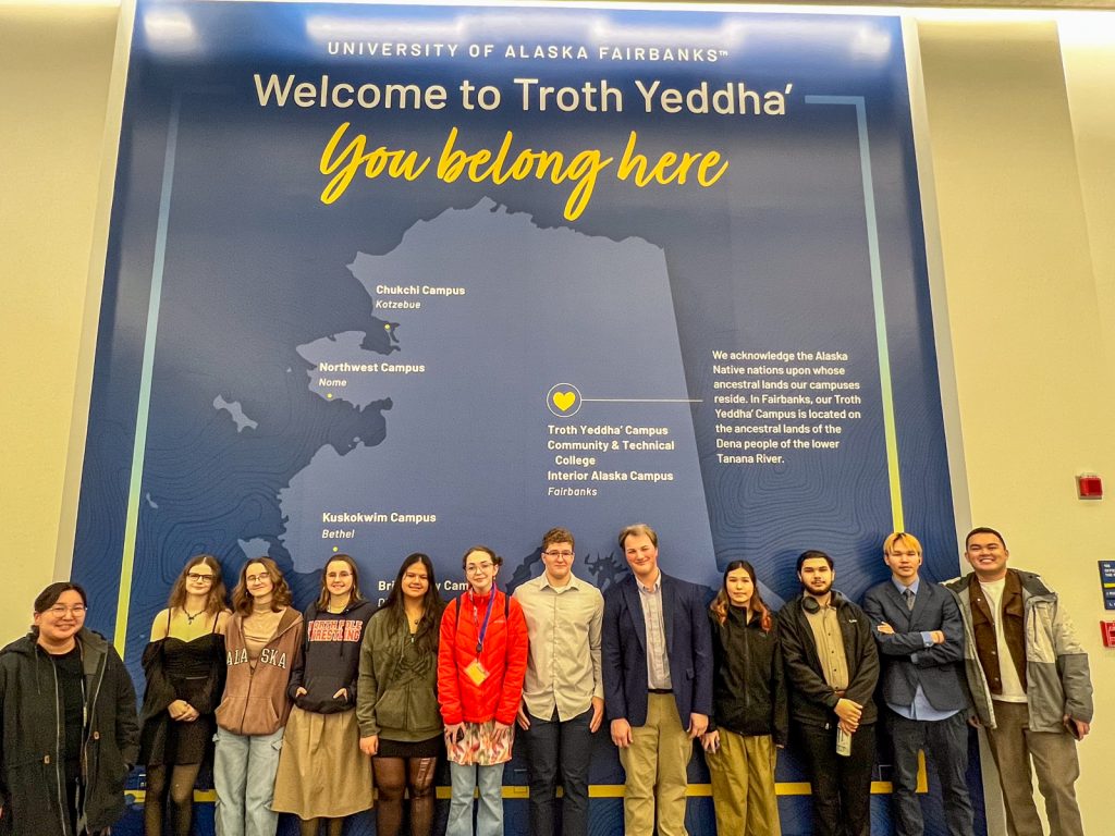 A group of students and staff posing in front of a banner, "You belong here"