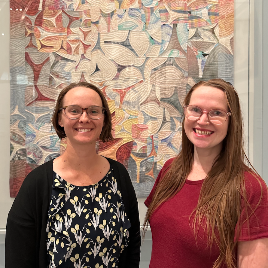 Della and Nic stand in front of a quilt