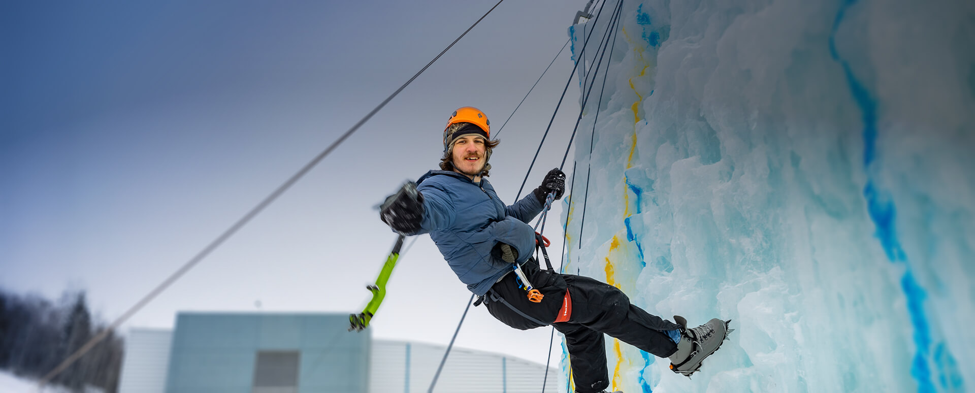 image of student climbing the ice wall and smiling at the camera