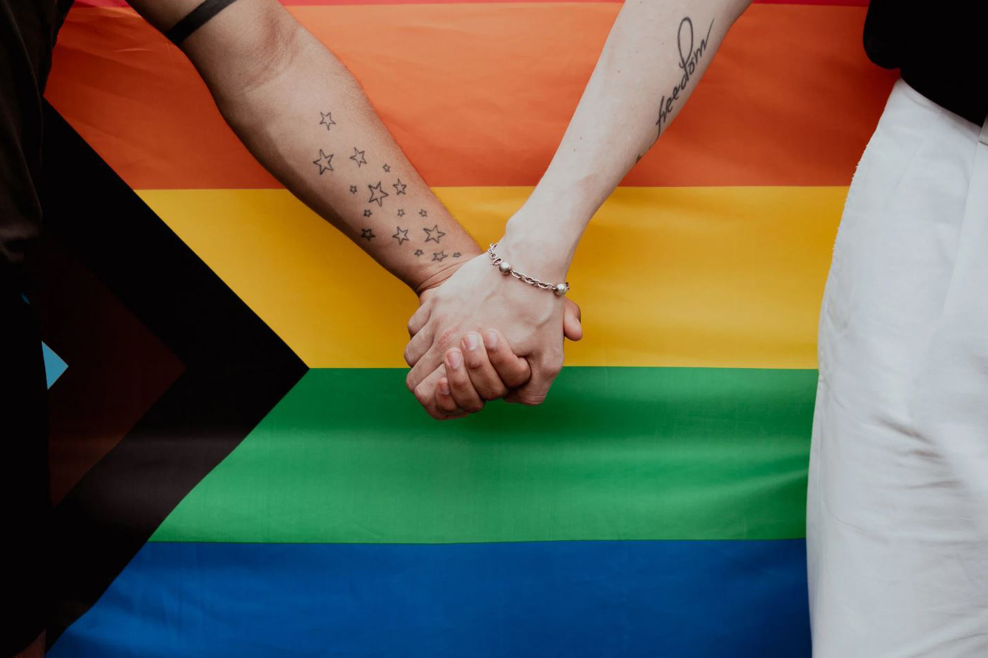 Two people hold hands in from of a New Progress Pride flag | Stock Photo from Canva